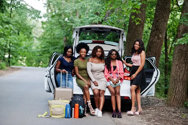 Friends sitting together by a car on a day out